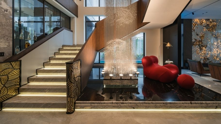 Sảnh thang bộ ấn tượng với thác nước pha lê lấp lánh, kết hợp ghế sofa đỏ biểu tượng và nội thất gỗ tối màu, tạo điểm nhấn luxury tại khu vực tiếp khách SEN Villa